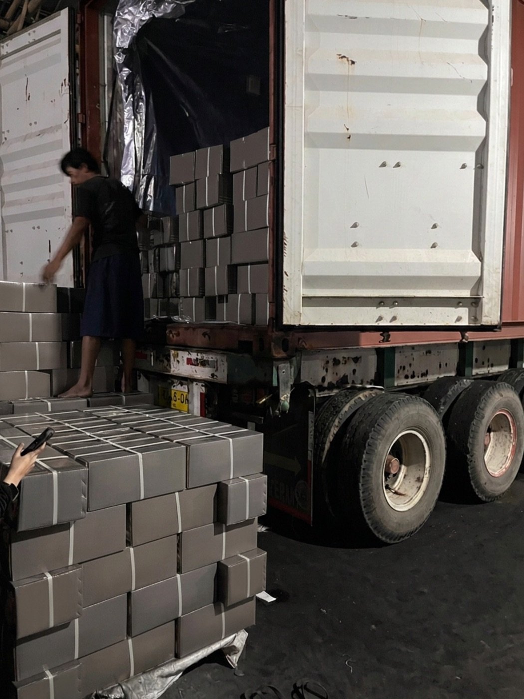 Worker stuffing master cartons of charcoal into an export container